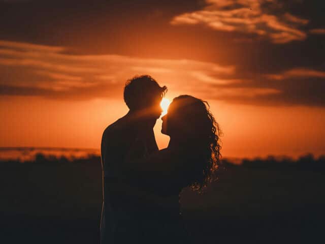 Couple enlacé avec un coucher de soleil au fond et un ciel orangé