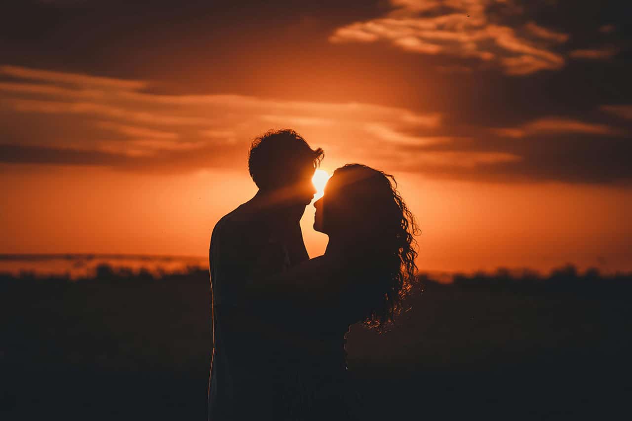 Couple enlacé avec un coucher de soleil au fond et un ciel orangé