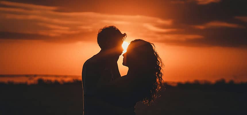 Couple enlacé avec un coucher de soleil au fond et un ciel orangé