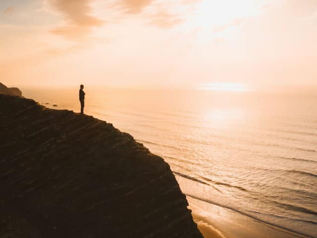 Belle vue d'une personne debout sur une falaise sur l'océan au coucher du soleil en Algarve, au Portugal