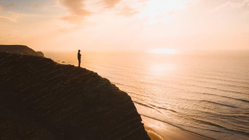 Belle vue d'une personne debout sur une falaise sur l'océan au coucher du soleil en Algarve, au Portugal