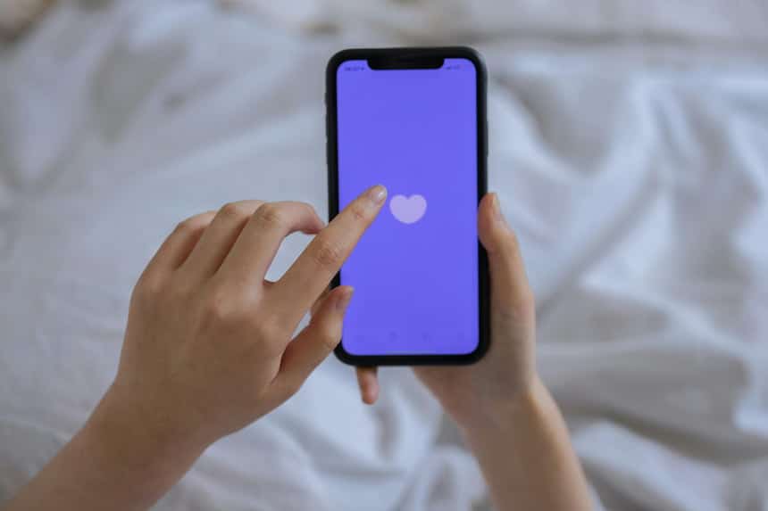 Main droite tenant un smartphone avec un cœur sur l'écran, main gauche touchant l'écran avec l'index