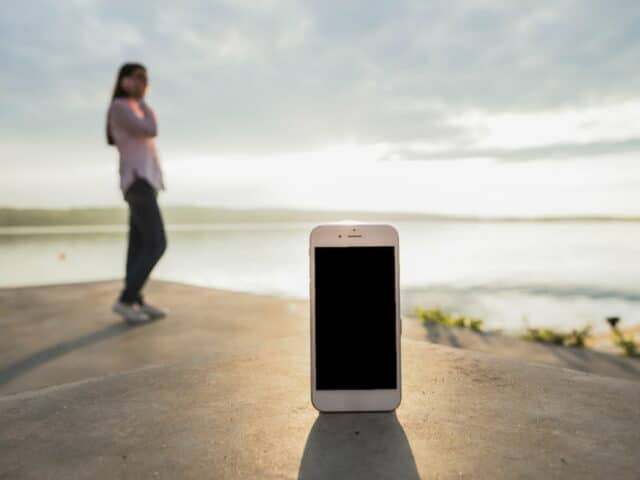 Smartphone au premier plan avec une jeune fille téléphonant en extérieur en arrière plan, un peu flouté