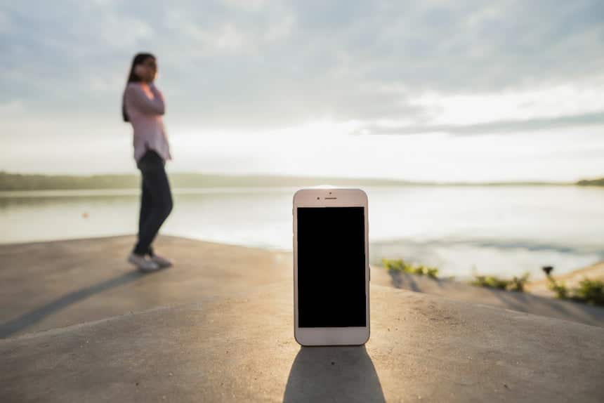 Smartphone au premier plan avec une jeune fille téléphonant en extérieur en arrière plan, un peu flouté