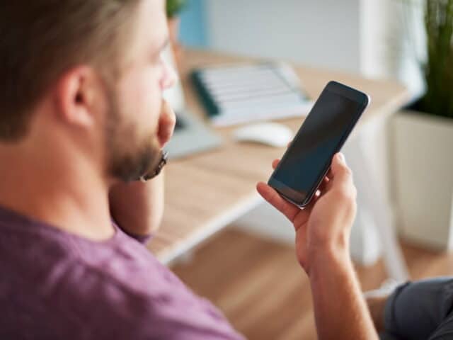 Homme flouté de trois-quart dos, tenant et regardant son smartphone