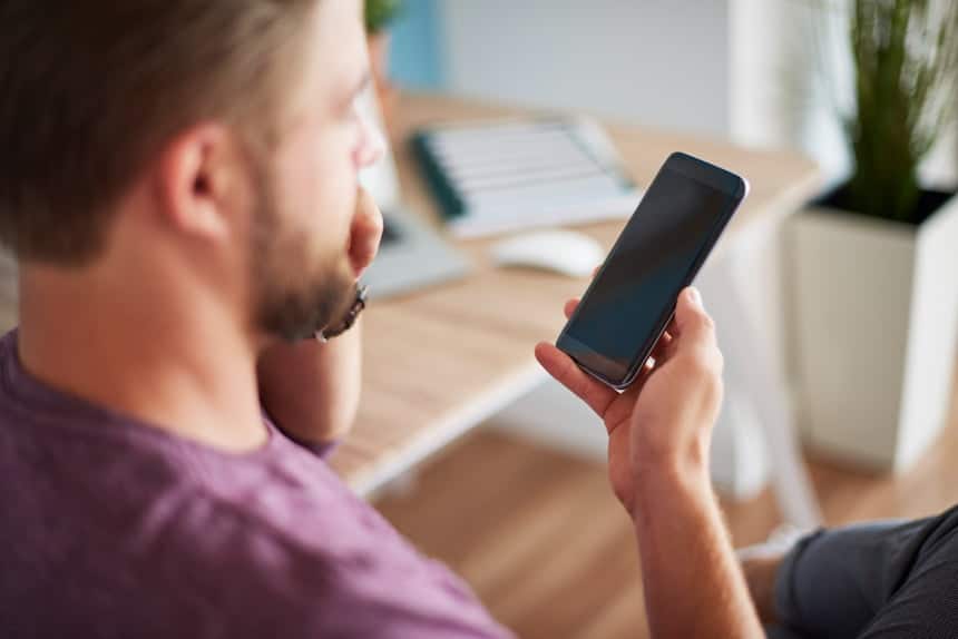 Homme flouté de trois-quart dos, tenant et regardant son smartphone
