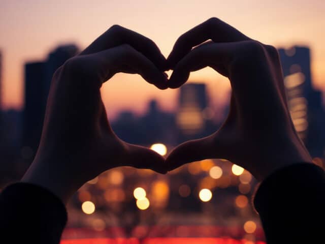 Deux mains opposées formant un coeur, avec un paysage urbain flouté en arrière plan