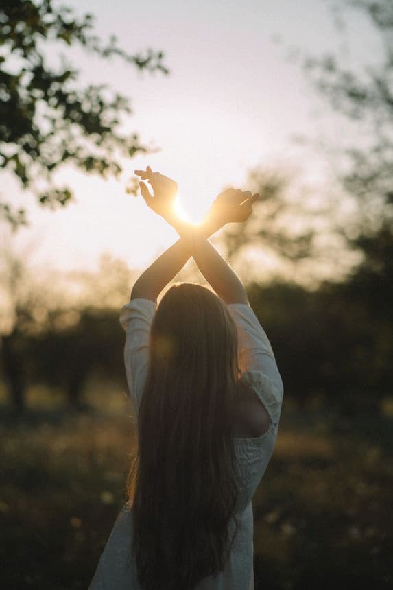 Femme de dos, les mains croisées vers en l'air, avec un lever de soleil en arrière plan