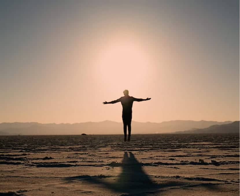 Silhouette d'une personne de dos ouvrant les bras, le soleil éclatant se dessinant derrière elle