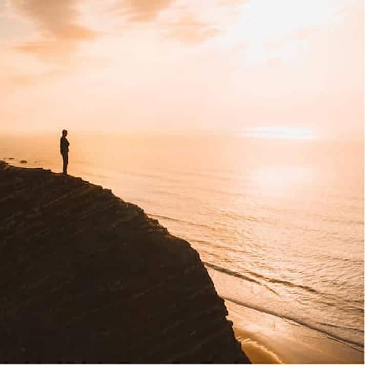Belle vue d'une personne debout sur une falaise sur l'océan au coucher du soleil en Algarve, au Portugal